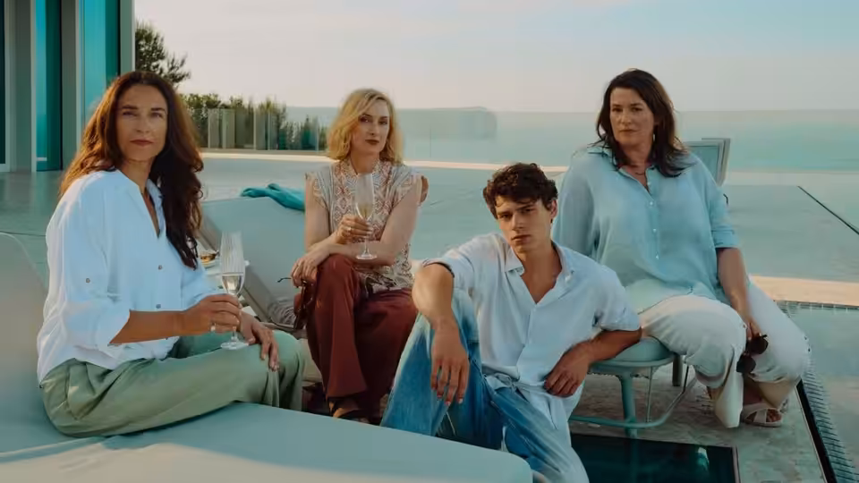 Three women and a young man sit beside a swimming pool at a modern house