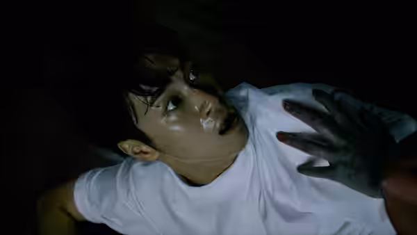 A young man lies on the floor as a dark hand reaches toward his chest