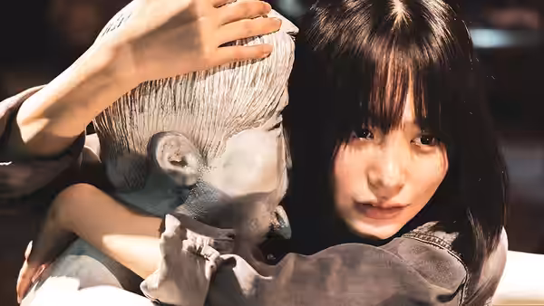 A young woman holds a pale sculpted head close against her shoulder
