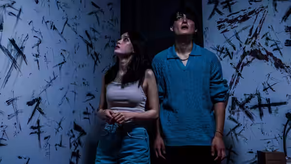 A woman and man stand beneath dense black markings on the walls, looking upward