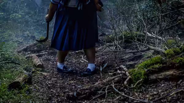 A schoolgirl grips a curved sickle on a wooded path