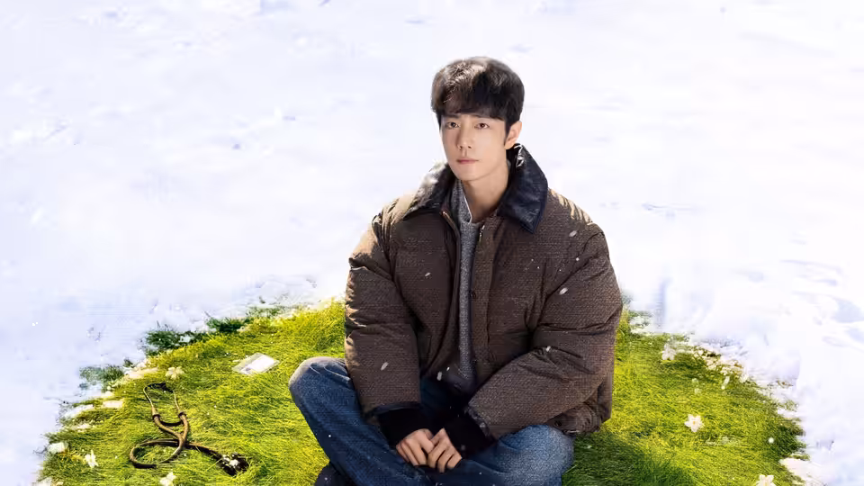 A young man sits on a patch of grass surrounded by snow