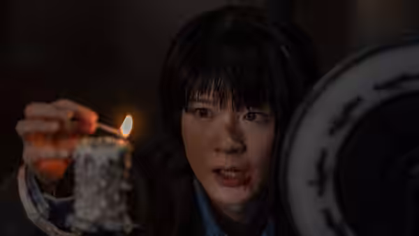A bloodied woman lights a candle beside an ornate circular object