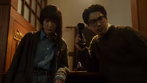 A woman and bespectacled man peer down, holding an old telephone receiver