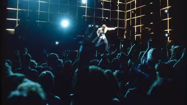 George Michael gestures to a cheering crowd beneath a grid of stage lights