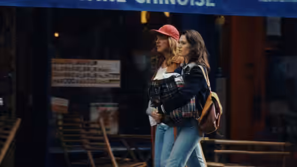A pregnant woman and her companion walk arm in arm past a shop