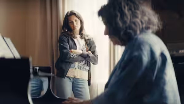A woman stands with folded arms as another person plays piano