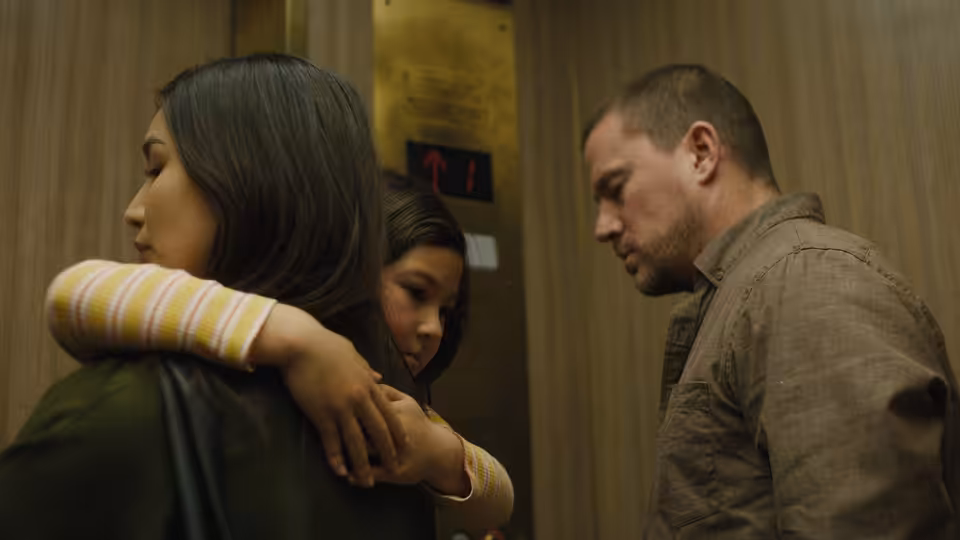 A woman embraces a young girl in an elevator as a man watches