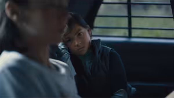 A young girl sits in a car, looking toward a man beside her