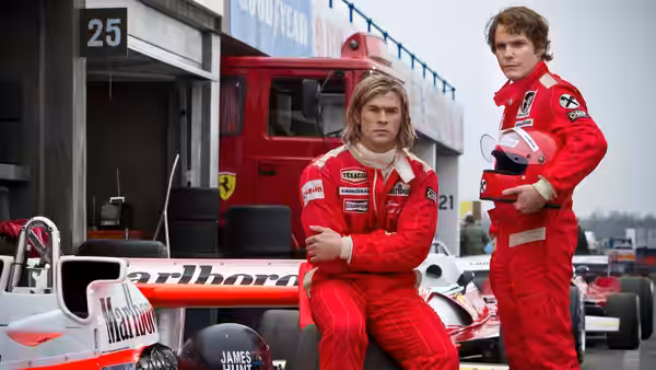 James Hunt (Chris Hemsworth) seated on tire beside Niki Lauda (Daniel Brühl) in pit lane