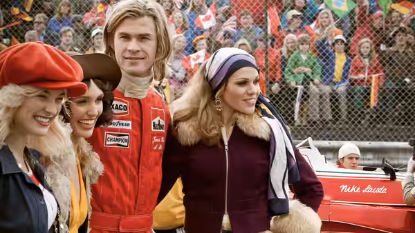 James Hunt (Chris Hemsworth) standing with three women beside a red car
