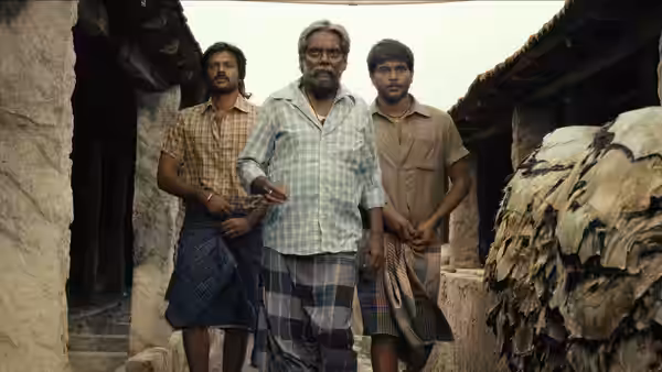 An older man leads two younger men through a narrow village lane