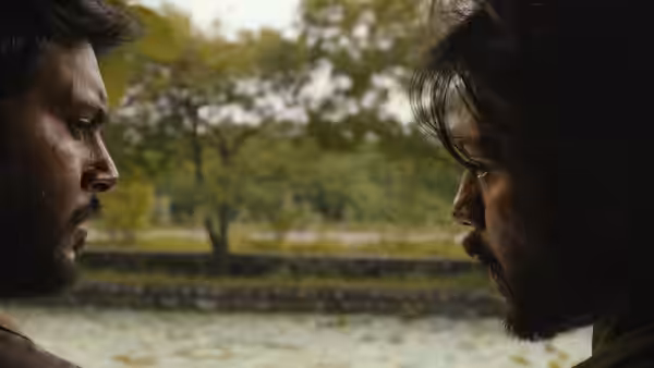 Two bearded men face each other closely beside a tree-lined pond