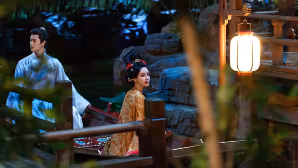 A robed man and woman ride a wooden boat through a rocky garden pond