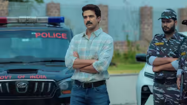 Ajay Dixit (Manoj Bajpai) stands with folded arms beside police vehicles and a uniformed guard