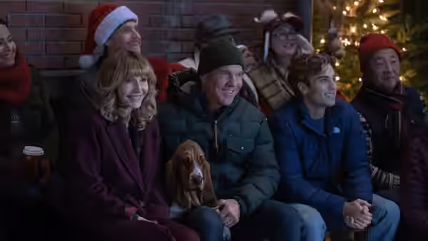 A family sits with a dog beside a Christmas tree, watching something offscreen