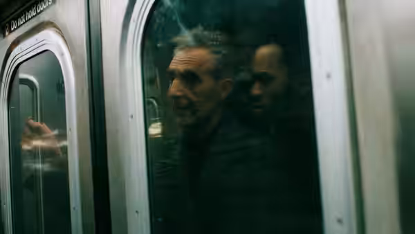 A man reaches toward a subway door, his face reflected in its window