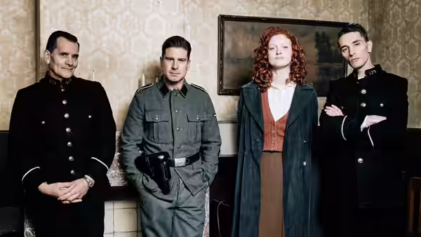 Two uniformed men, a red-haired woman, and another man stand together in a decorated room