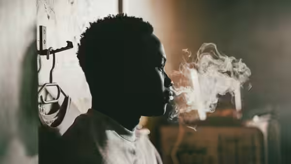 A young man exhales cigarette smoke beside a wall-mounted coat hook