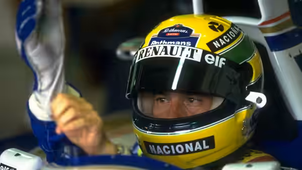 Ayrton Senna in a yellow helmet seated in the cockpit