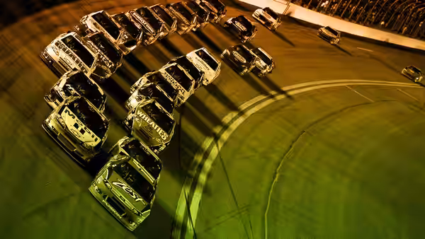 a pack of stock cars lined up on the racetrack at dusk