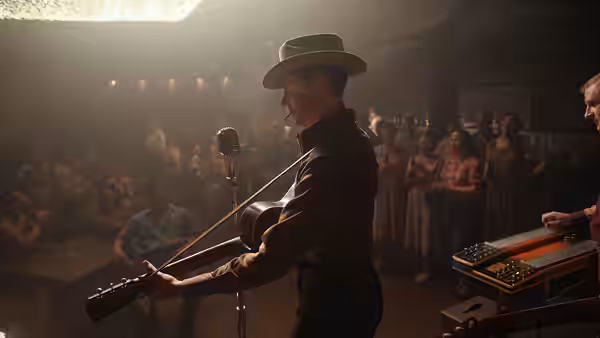 Hank Williams (Tom Hiddleston) plays guitar at a microphone before a seated audience