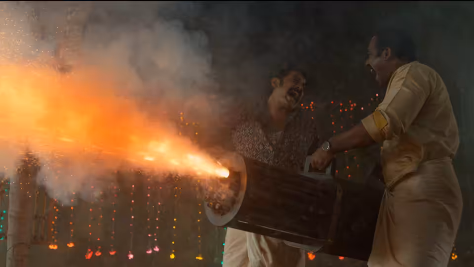Two men operate a large firework launcher as sparks and smoke erupt across a festive gathering