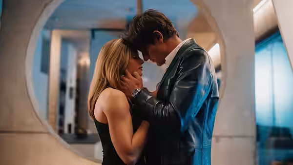A man gently holds a woman's face as they embrace beneath a circular doorway