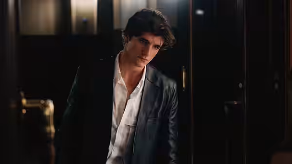 A young man in a leather jacket stands in a dark doorway