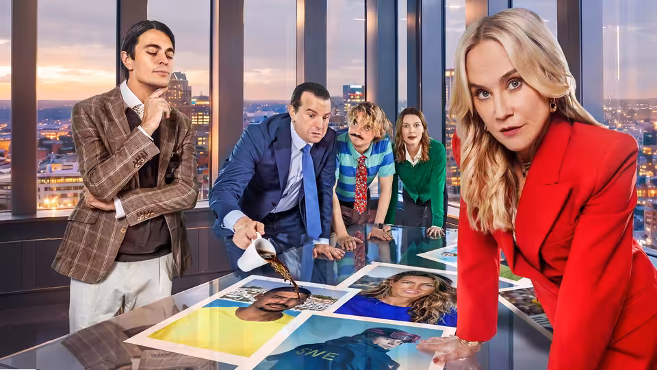 A blonde woman in red leans over a table of portraits as coworkers study them