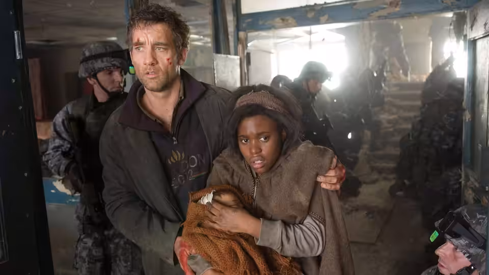 Theo Faron (Clive Owen) and Kee (Clare-Hope Ashitey) shield the baby from armed soldiers in a ruined corridor