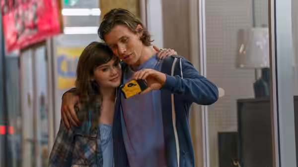 Charlie (Nick Robinson) puts an arm around Harper (Emilia Jones) and shows her a yellow object