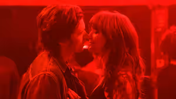 Charlie (Nick Robinson) and Harper (Emilia Jones) lean in close beneath red lights