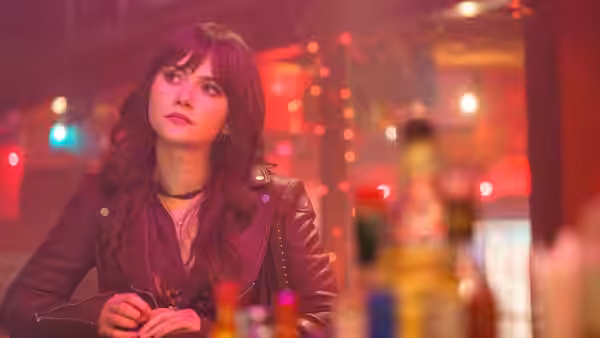 Harper (Emilia Jones) sits at a bar, holding a drink beneath neon lights