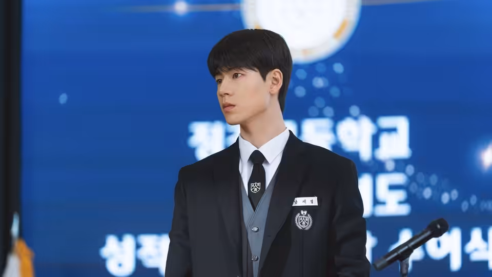 A student in uniform stands beside a microphone before a blue event backdrop