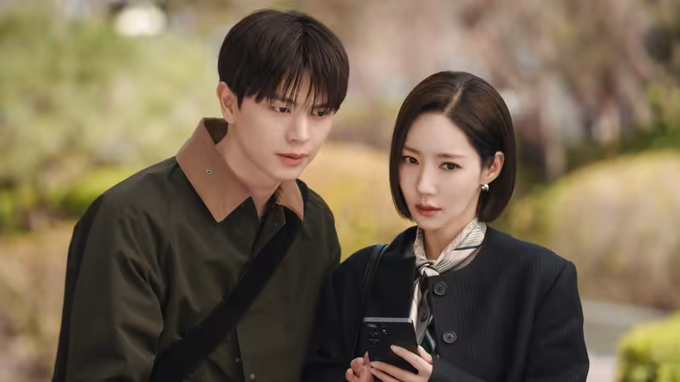 A woman and a man stand outdoors, studying a phone together