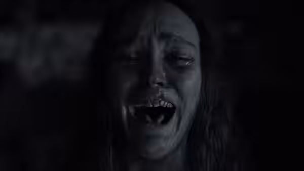 A long-haired woman screams, revealing sharp pointed teeth