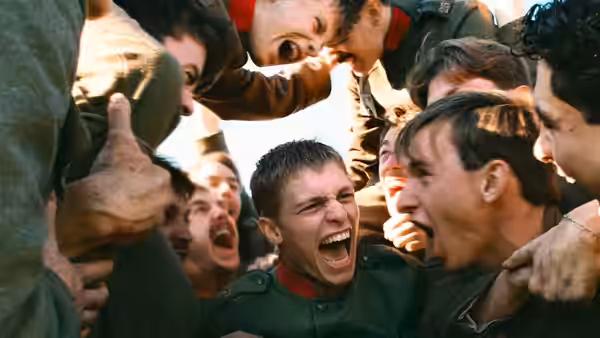 A young uniformed soldier shouts as fellow soldiers crowd around him
