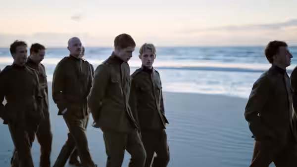 A group of uniformed soldiers walks along the beach beside the water