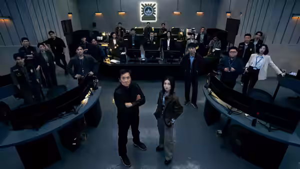 A group gathers around a central desk in a control room