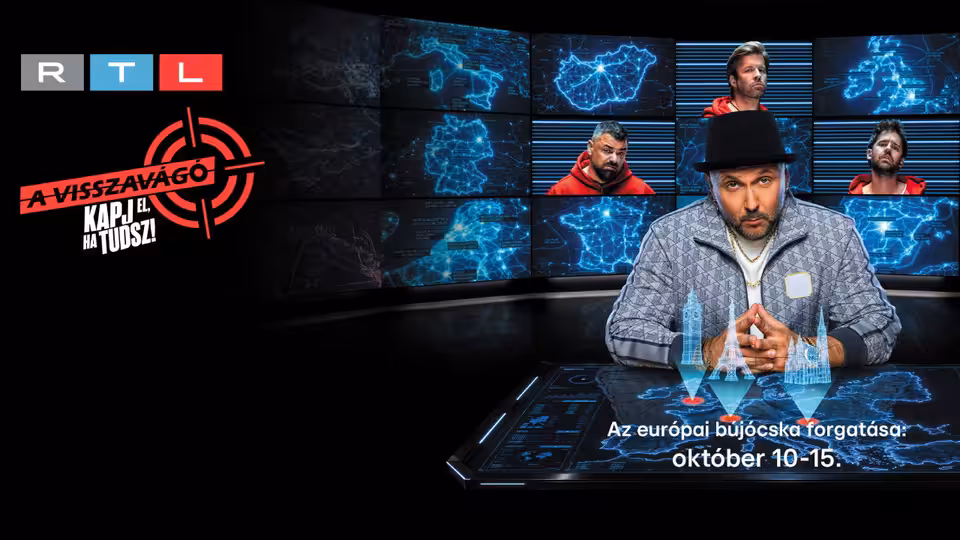A man in a black hat sits at a control desk before surveillance monitors