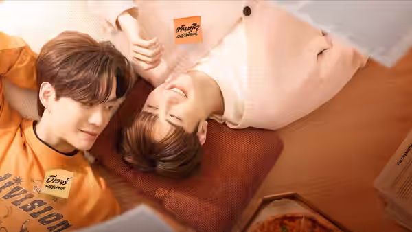 Two people in orange and pale pink shirts lie side by side on a wooden floor