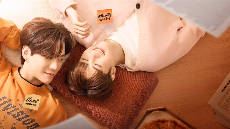 Two people in orange and pale pink shirts lie side by side on a wooden floor