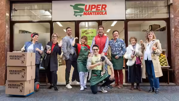 A group of shop workers pose outside a supermarket beside stacked potato boxes
