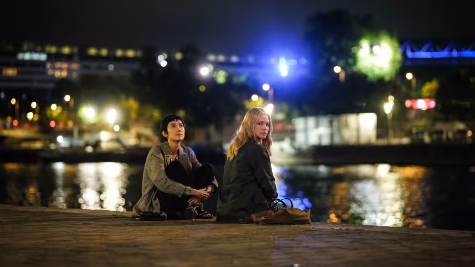 Marie Lou-Fontaine (Virginie Efira) and Mari Morisaki (Tao Okamoto) sit beside a river at night
