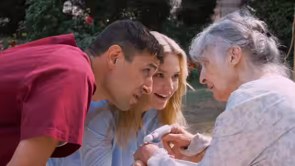 A man and Marie Lou-Fontaine (Virginie Efira) lean close to an elderly woman outdoors
