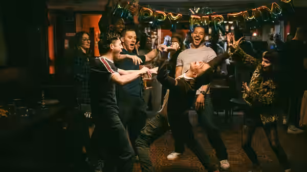 Friends dance and cheer together in a crowded pub beneath party decorations