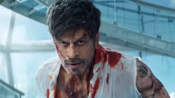 A bloodied man leans forward inside a glass-walled modern building