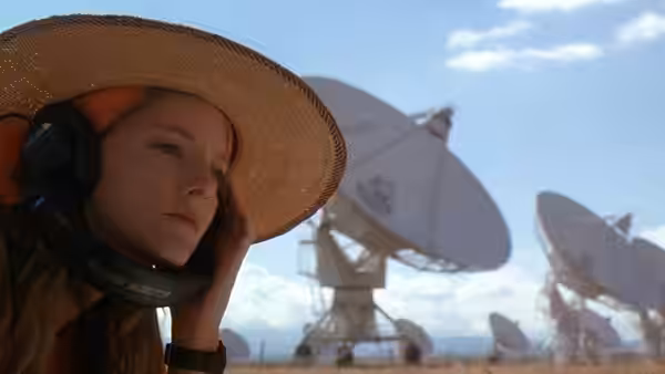A young girl listens intently at a vast radio telescope facility