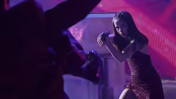 Eve (Ana de Armas) aiming a pistol at a figure in a neon nightclub